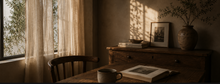 Warm reading corner with wooden desk, open book, coffee cup and soft sunlight through linen curtains