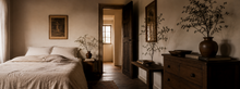 Warm rustic bedroom with linen bedding, dark wood beams and soft natural light through an open doorway