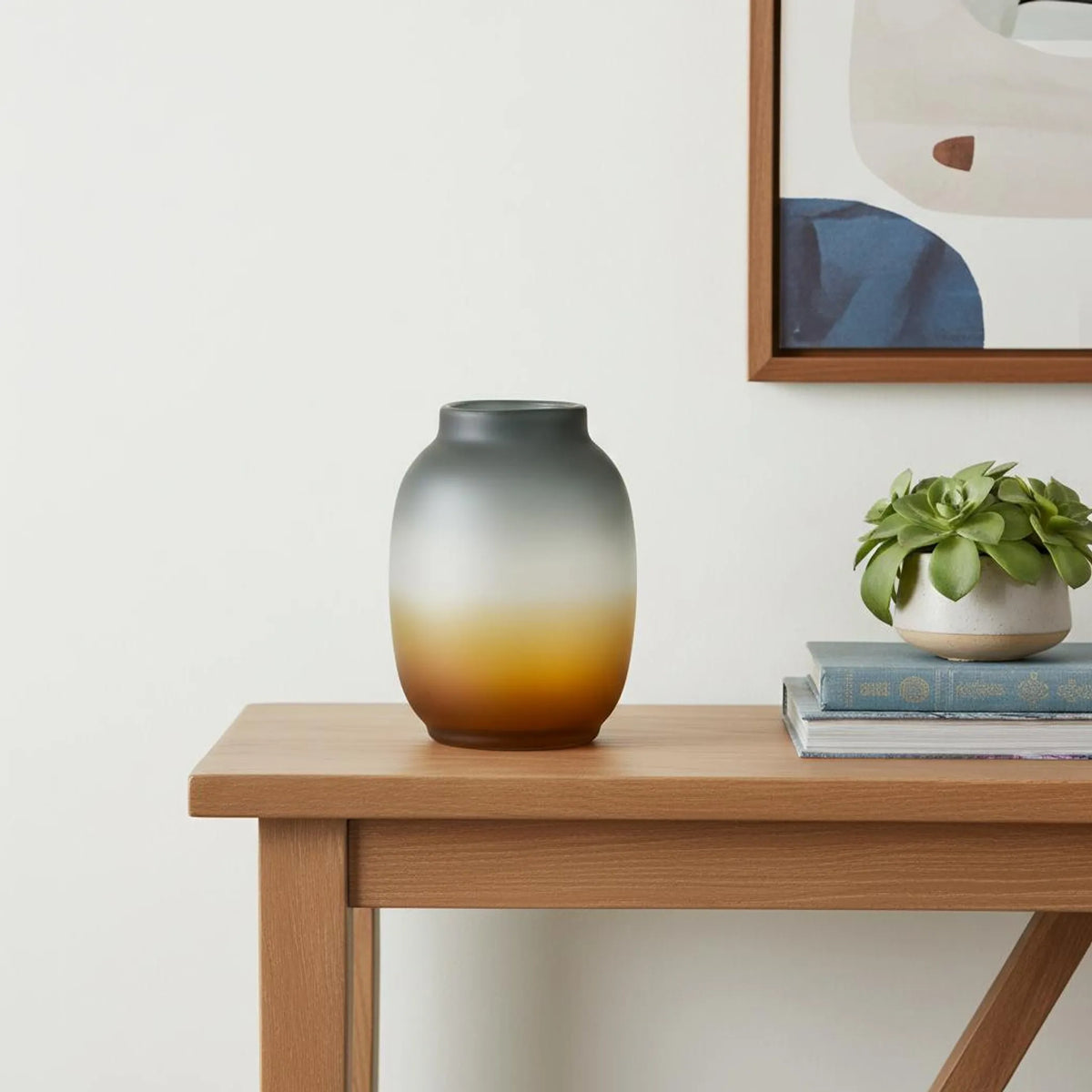 Ombre glass table vase in gray-to-amber gradient, styled on wood console table with plant and books