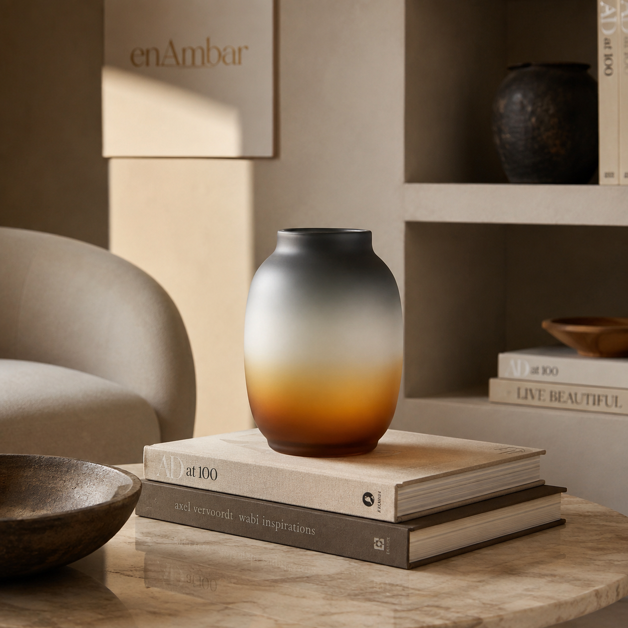Round charcoal and amber glass table vase displayed on design books in a warm modern interior.