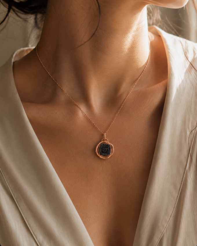Close-up of a woman wearing a rose gold pendant necklace with a dark stone, styled with an ivory satin blouse.