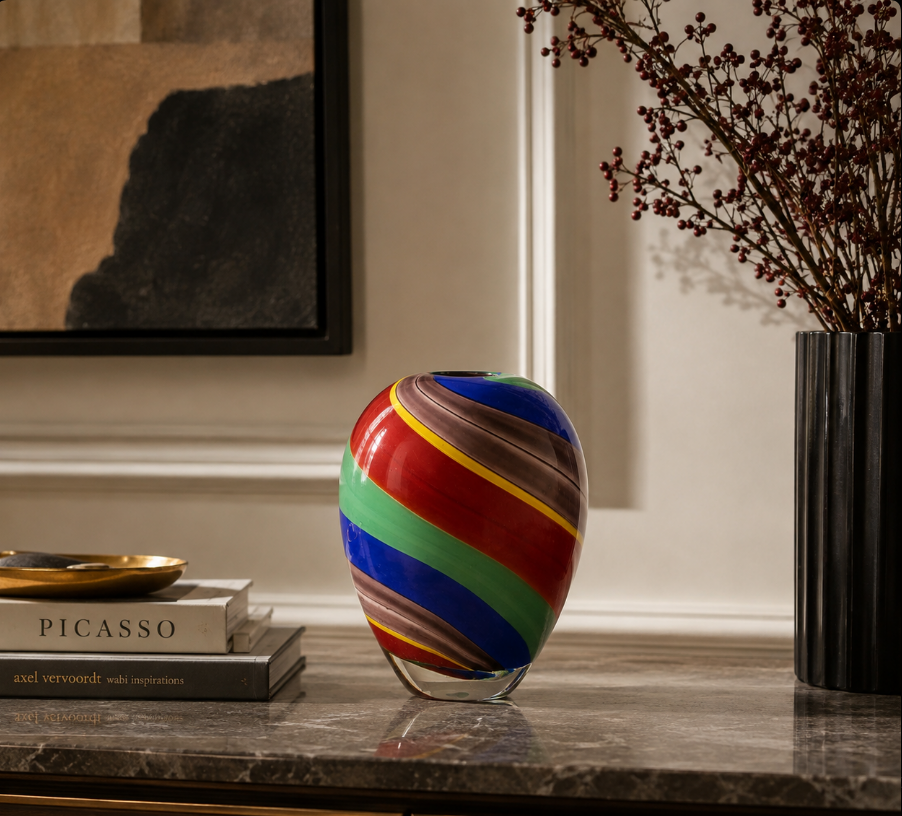 Colorful striped glass vase displayed on a marble console beside art books in a refined contemporary interior.